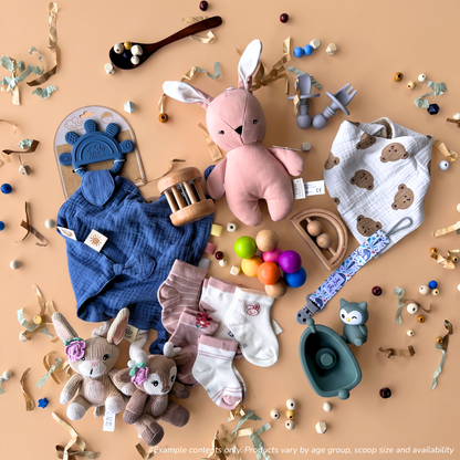 A styled flat-lay of 0-6 Month baby sensory gift box items, including a pink Living Textiles plush linen bunny, a Living Textiles blue teething comforter, a Spillykins dribble bib, a My Little Giggles wooden teething toy, Totli colorful grasping balls, a Living Textiles bath toy, Spillykins cotton socks, Zebra Babies dummy clip, Montessori Mates baby's first silicone cutlery set, and Living Textiles woodland-themed pram toy.