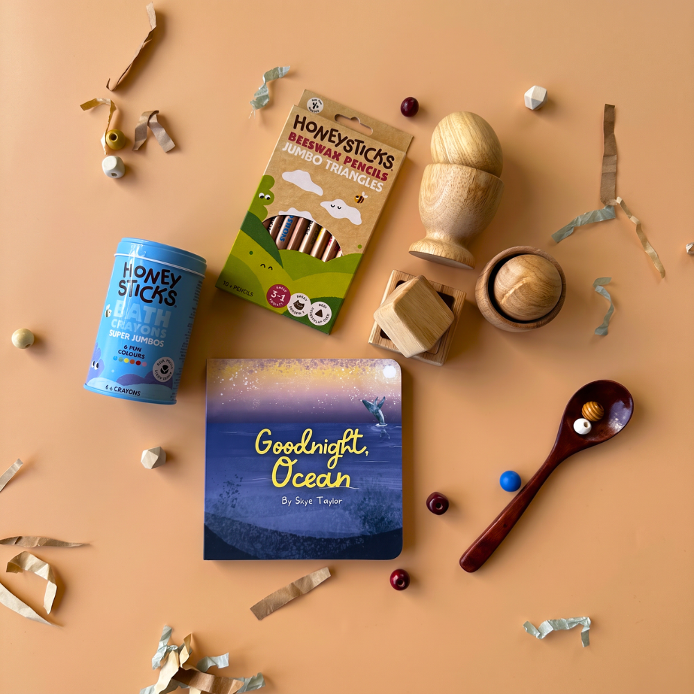 12-24 Month baby and toddler sensory gift box flat-lay including bath crayons from Honeysticks, jumbo pencils from Honeysticks, Egg, Ball & Cup Set from Q Toys, and a Board Book from Loose Parts Press.