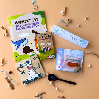 2-3 Year toddler sensory gift flat-lay of a 1-scoop order, showing a colouring book from Honeysticks, jumbo pencils from Honeysticks, magnesium bath bombs from Mindful & Co. Kids, a zebra chunky puzzle from Zookabee, and eco-friendly playdough from Play Sense.