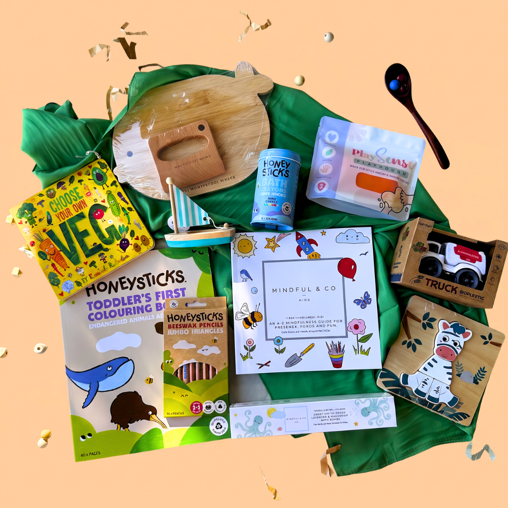 2-3 Year toddler gift box flat-lay of a 2-scoop order showing 1 board book from Loose Parts Press, green play silk from Play Silkies, Wooden KidsCutting Board and knife Set from Montessori Mates, eco-friendly playdough from Play Sense, colouring book from Honeysticks, jumbo colouring pencils from Honeysticks, magnesium bath bombs from Mindful and Co. Kids, a Bioplastic truck from Jiggle & Giggle, wooden toy sail boat from Toyslink, a Mindful & Co kids colouring book, and bath crayons from Honeysticks.