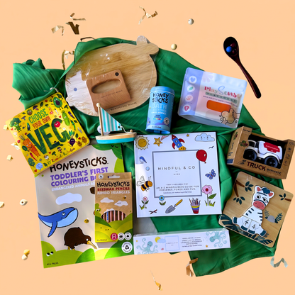2-3 Year toddler gift box flat-lay of a 2-scoop order showing 1 board book from Loose Parts Press, green play silk from Play Silkies, Wooden KidsCutting Board and knife Set from Montessori Mates, eco-friendly playdough from Play Sense, colouring book from Honeysticks, jumbo colouring pencils from Honeysticks, magnesium bath bombs from Mindful and Co. Kids, a Bioplastic truck from Jiggle & Giggle, wooden toy sail boat from Toyslink, a Mindful & Co kids colouring book, and bath crayons from Honeysticks.
