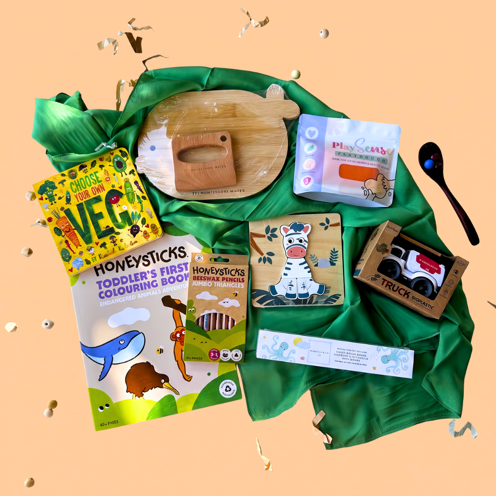 2-3 Year toddler gift box flat-lay of a 2-scoop order showing 1 board book from Loose Parts Press, green play silk from Play Silkies, Wooden KidsCutting Board and knife Set from Montessori Mates, eco-friendly playdough from Play Sense, colouring book from Honeysticks, jumbo colouring pencils from Honeysticks, magnesium bath bombs from Mindful and Co. Kids, and a Bioplastic truck from Jiggle & Giggle.