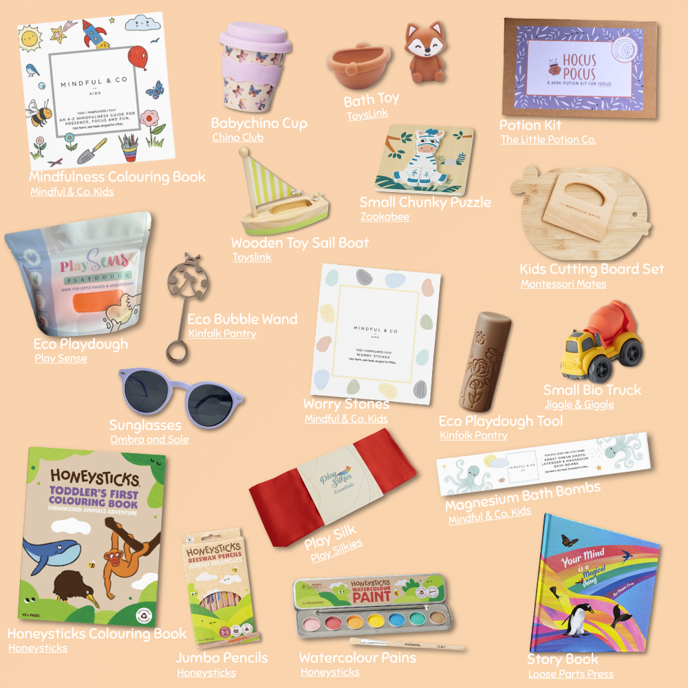 A flat-lay collage of multiple handcrafted and branded stationery, craft, and toy products arranged on a warm beige background. Visible items include a Mindfulness Colouring Book, Babychino Cup, Bath Toy, bath bombs, Small Chunky Puzzle, Wooden Toy Sail Boat, Eco Bubble Wand, Kids Cutting Board Set, Honeysticks Colouring Book, Jumbo Pencils, Watercolour Paints, and other small gift items, each labeled with its brand.