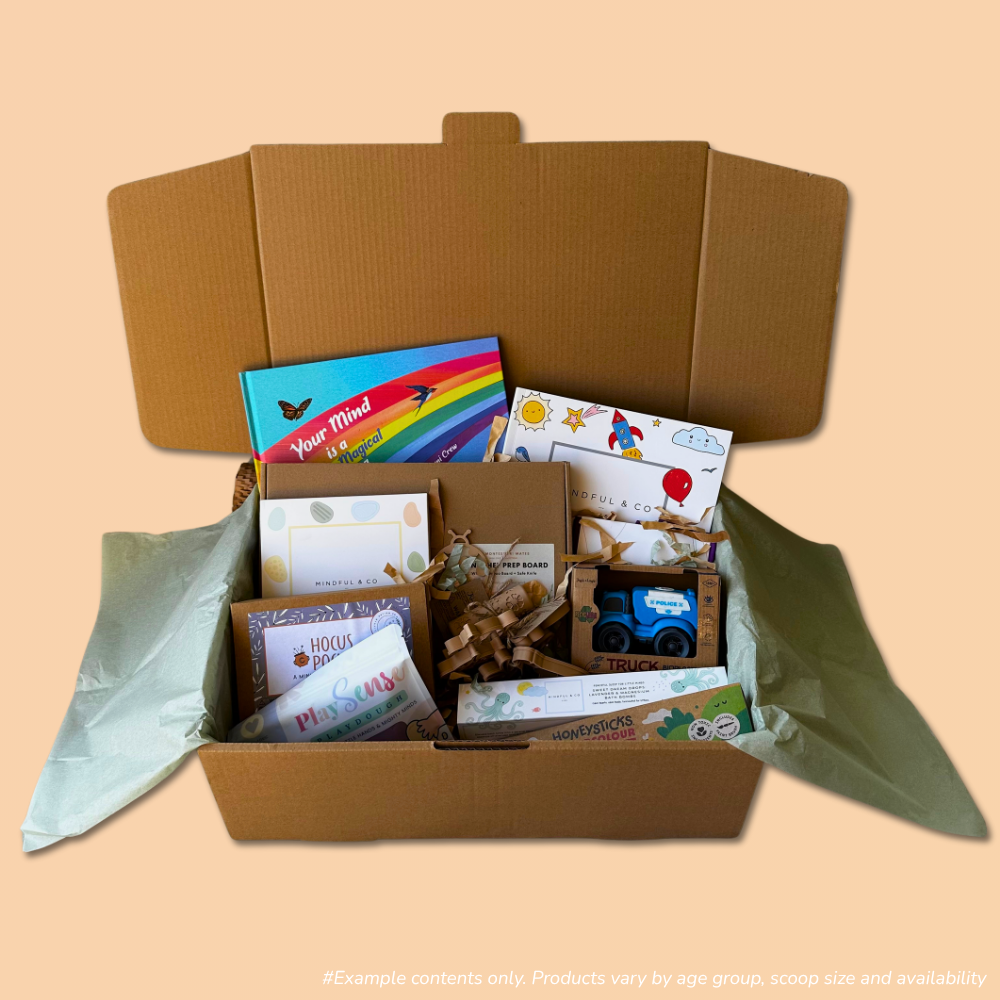 An open cardboard gift box filled with assorted children's items from the 3-5 year scoop order, including a story book, colouring books, a small bioplastic truck, and eco-friendly playdough and playdough tools, set against a solid peach background.