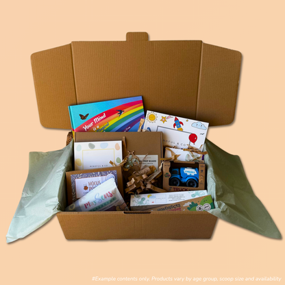 An open cardboard gift box filled with assorted children's items from the 3-5 year scoop order, including a story book, colouring books, a small bioplastic truck, and eco-friendly playdough and playdough tools, set against a solid peach background.