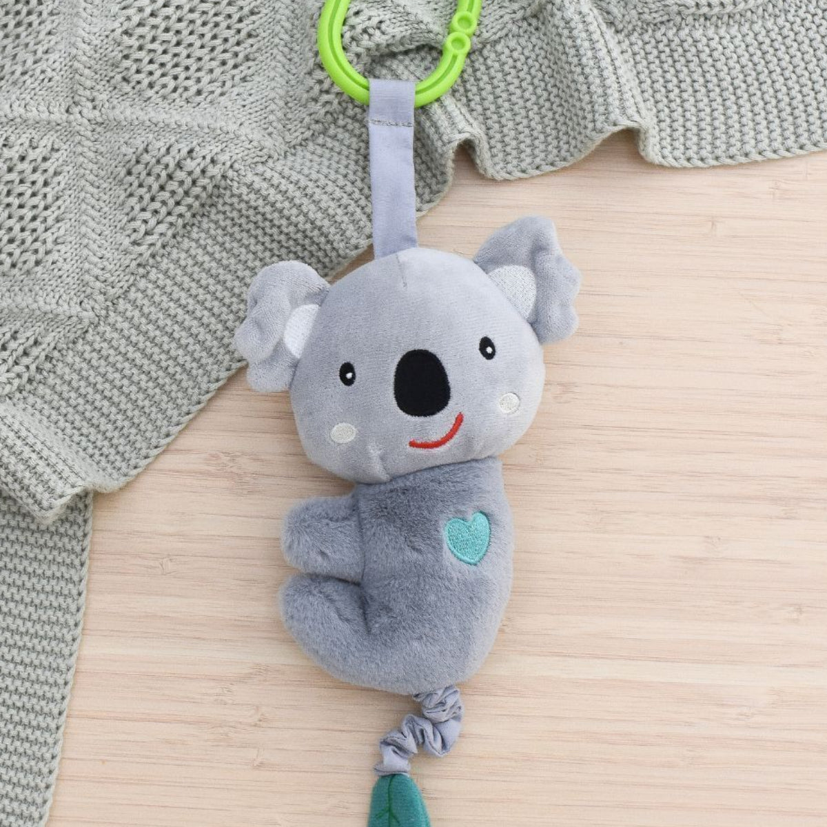 Gray koala plush toy with a green leaf on a textured surface with a gray blanket.