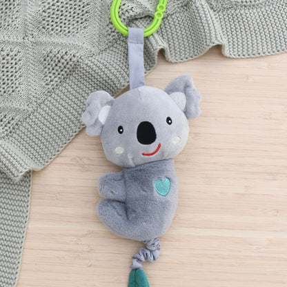 Gray koala plush toy with a green leaf on a textured surface with a gray blanket.
